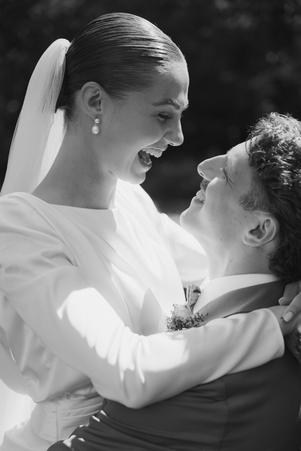 Braut und Bräutigam lachen sich liebevoll an, während sie sich umarmen – ein emotionaler Moment in Schwarz-Weiß, festgehalten an ihrem Hochzeitstag.