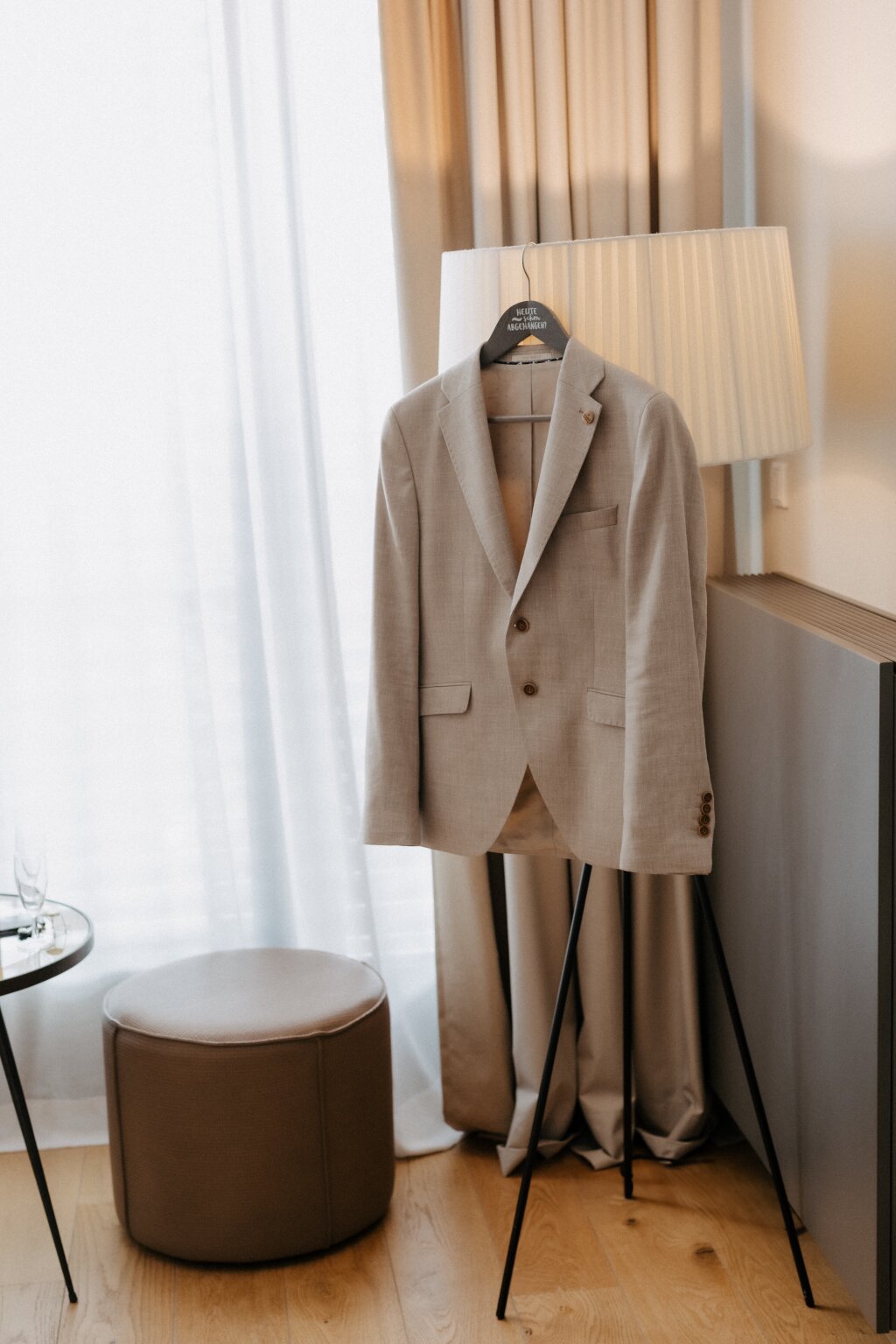 Beiger Hochzeitsanzug des Bräutigams auf Kleiderbügel im Hotelzimmer.