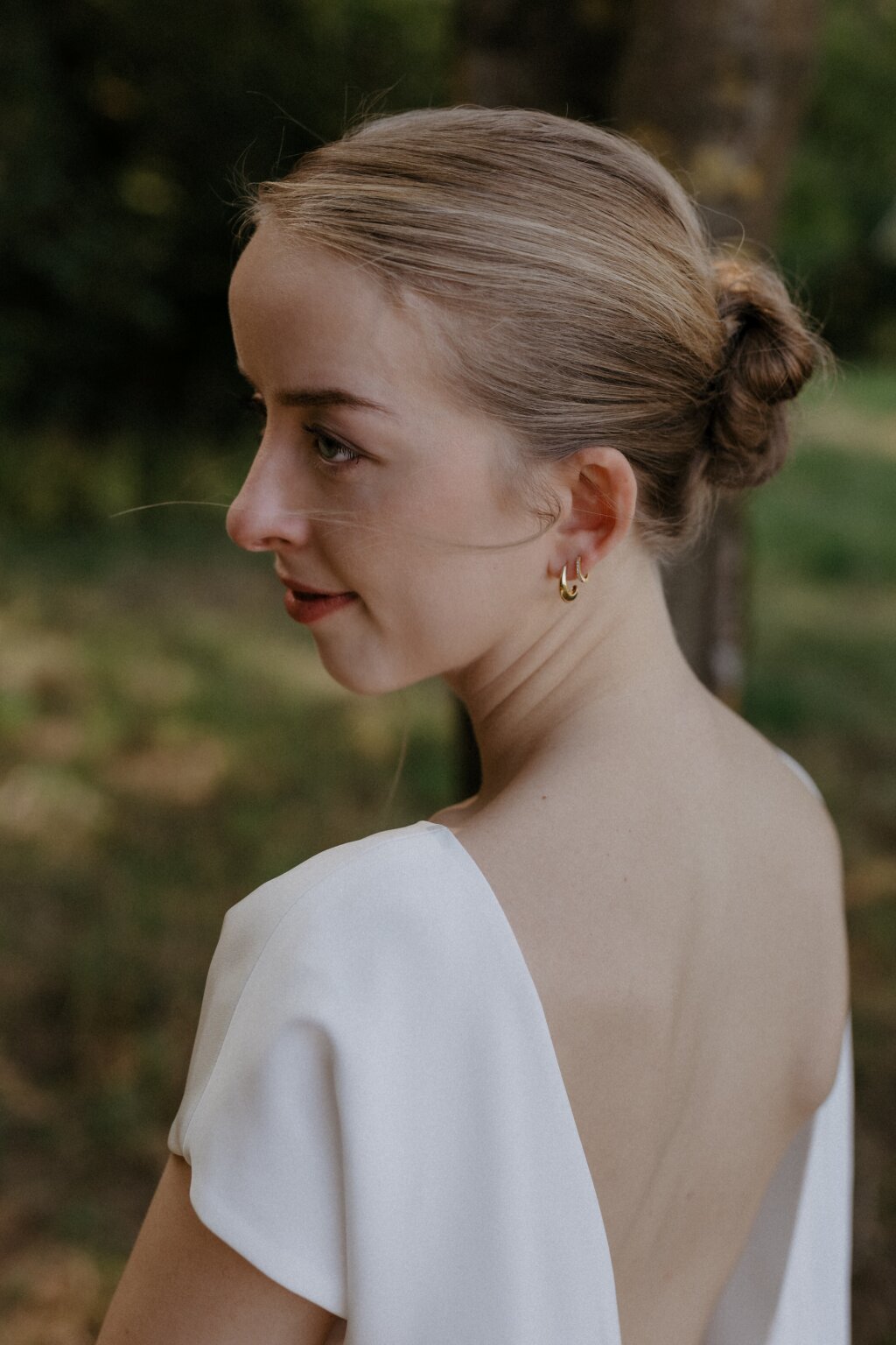 Nahaufnahme der Braut mit zurückgestecktem Haar und goldenen Ohrringen im natürlichen Licht.