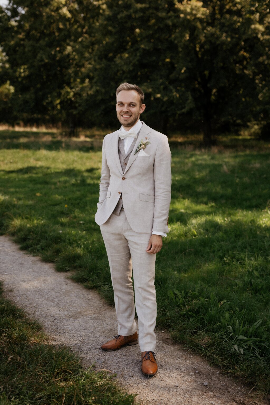 Der Bräutigam steht locker und lächelnd auf einem Waldweg – elegantes Hochzeitsfoto.