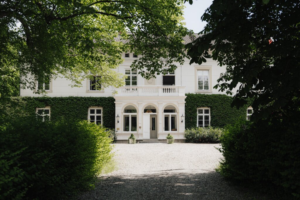 Romantische Einfahrt zu einem eleganten weißen Herrenhaus mit bewachsenen Fassaden – perfekte Kulisse für eine Hochzeitsfeier.