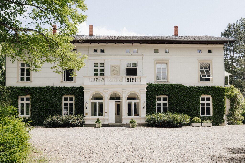 reite Ansicht des weißen Herrenhauses mit freiem Platz davor – ideal für Empfang oder Outdoor-Trauzeremonie.